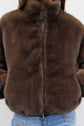 A person wearing a brown parka courte en fausse fourrure with a zipper, partially zipped up, and blue jeans.