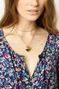 A woman wearing a floral-patterned blouse, layered gold necklaces, and a gold heart locket. Only the lower half of her face and upper torso are shown.