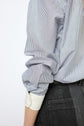 A person wearing a blue and white chemise rayée in popeline coton with rolled-up sleeves and dark jeans, shown from the back. The image focuses on the shirt’s fabric—highlighting the crisp popeline coton—and the person’s left arm and side, drawing attention to the smart col blanc.