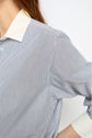 A close-up of a person wearing a blue and white popeline coton chemise rayée with a crisp col blanc and white cuffs, their arm bent at the elbow.