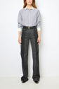 A person stands against a white background wearing a blue-gray popeline coton button-up shirt with col blanc and white cuffs, paired with high-waisted black jeans featuring large front pockets and black shoes. Their face is not visible.