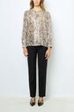 A person wears a long-sleeve, floral blouse with black dress pants and black pointed-toe shoes, standing against a plain white background.