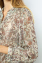 A person wearing a long-sleeved, light-colored blouse with a brown and green floral pattern, showing the upper body and arm, with light brown hair visible.