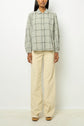 A person wearing a gray plaid button-up shirt with puffy sleeves and beige wide-leg pants, standing against a plain white background.