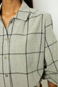 Close-up of a person wearing a light gray plaid shirt with black and yellow lines. The shirt has a collar, button-down front, and rolled-up sleeves. The persons face is not visible.