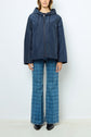 A person wearing a navy parka courte with capuche and blue plaid flared jeans, crafted using a polyester technique, stands facing forward against a plain white background.