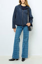 Person wearing a navy parka courte in polyester technique, blue plaid flared jeans, black pointed boots, and carrying a black shoulder bag, standing against a plain light background.