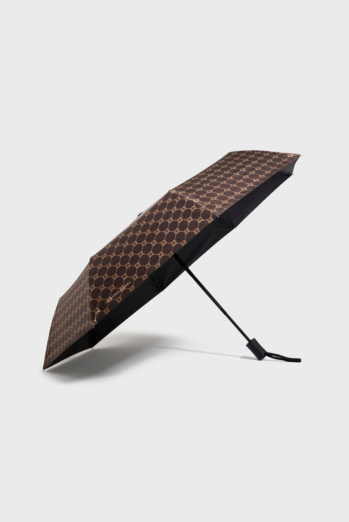 A brown parapluie pliant with a gold geometric pattern, partially open and resting at an angle on a light gray background. Featuring ouverture automatique for easy use, this umbrella combines style with convenience.