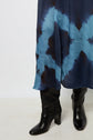 A person wearing knee-high black leather heeled boots and a blue and black tie and dye jupe midi, standing on a light-colored floor against a plain white background.