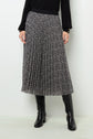 Woman wearing a black ribbed sweater, a pleated black midi skirt with a white floral pattern, and black knee-high boots, standing against a plain white background.