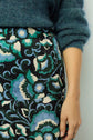 A person wearing a teal fuzzy sweater and a black skirt with a blue, white, and green floral pattern. Only the torso and one arm are visible.