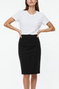Woman wearing a plain white short-sleeve t-shirt tucked into a high-waisted, knee-length jupe noire en laine, standing with hands on hips against a white background.