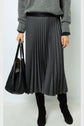 Person wearing a grey sweater, a black pleated skirt with small dots, black knee-high boots, and holding a large black handbag.