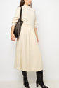 Woman wearing a cream-colored long-sleeve dress paired with black knee-high boots and a black shoulder bag, standing against a plain white background. Her elegant look is perfect for the season and reminiscent of classic jupe hiver femme style, blending timeless charm with modern simplicity.