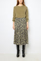 A woman wearing a fuzzy olive green sweater, a black floral midi skirt, and black knee-high boots stands against a plain white background. Her hands are at her sides and her head is slightly turned.