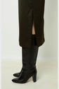 A person wearing a dark green skirt with a side slit and black heeled knee-high boots stands on a light-colored floor against a plain white background.