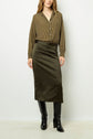 A person wearing a brown striped blouse, an olive green satin midi skirt, and black knee-high boots stands against a plain light background.