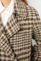 Close-up of a person wearing a textured manteau court à carreaux in brown and beige plaid over a white collared shirt. Only part of the face, shoulder, and torso are visible.