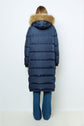 A person stands facing away, wearing a doudoune longue navy blue puffer coat with a fur-lined hood and blue jeans against a plain white background.