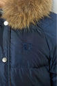 Close-up of a navy blue doudoune à capuche jacket with a fur collar, metal snap buttons, and an embroidered logo on the chest.