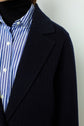Close-up of a person wearing a manteau rayé blue pinstripe blazer over a blue and white striped button-up shirt and a black turtleneck. Only the upper body is visible, with no face shown.