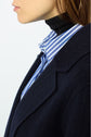Close-up of a person wearing a navy manteau droit, a blue and white striped shirt, and a black turtleneck. Only the lower half of their face and upper torso are visible.