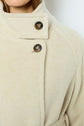 Close-up of a beige laine alpaga wool coat with two dark buttons on the collar. Part of a person’s face and hair is visible at the top left. The manteau mi-long features a soft texture and a structured design.