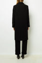 A person stands facing away, wearing a manteau droit long black coat crafted from pardessus laine vierge, paired with black pants and black shoes against a plain white background. Only the back view of this manteau mi-long femme is visible.