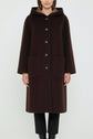 A person wearing a long, dark brown manteau à capuche with large front pockets and black buttons, standing against a plain white background.