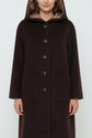 A person wearing a dark brown manteau à capuche with large buttons and front pockets, standing against a plain light background.