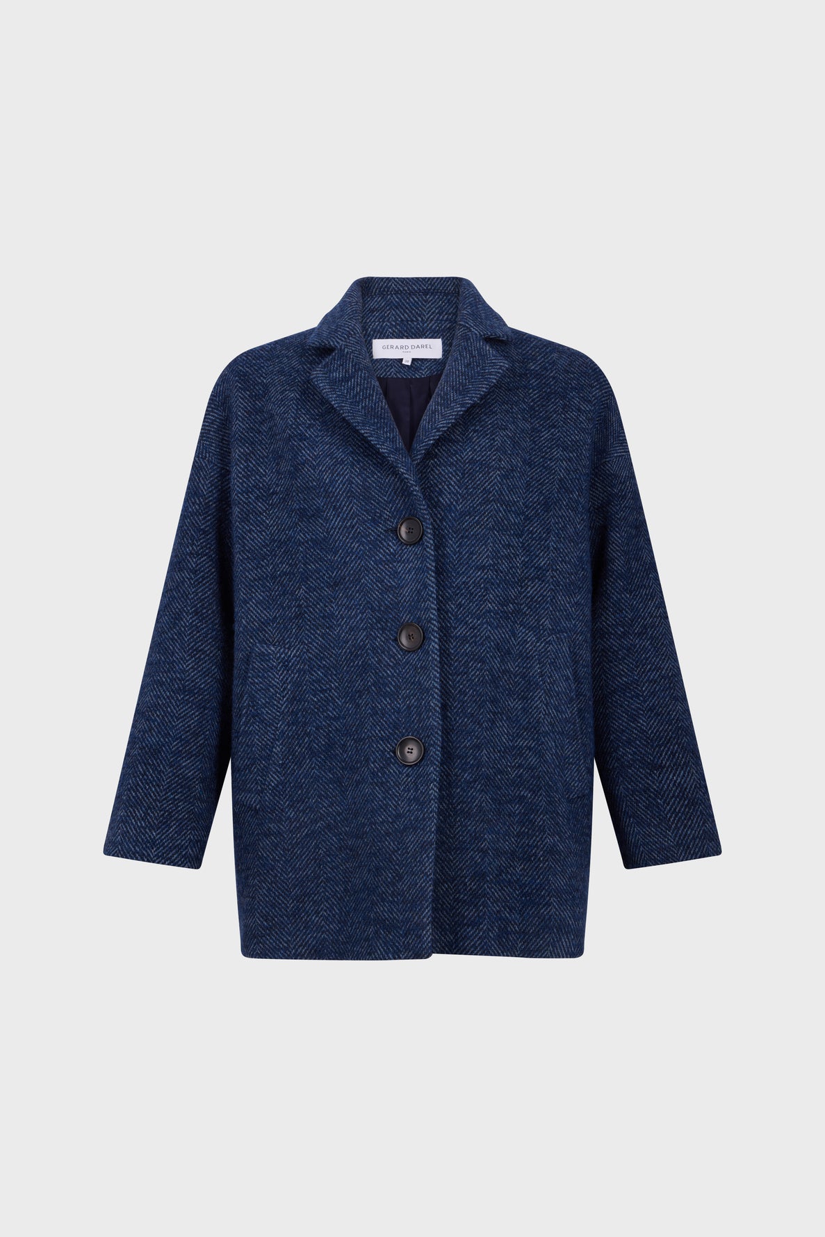 A navy blue, textured manteau à chevrons with three black buttons, wide lapels, and long sleeves, displayed on a plain light gray background.