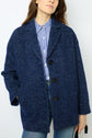 A person wearing a blue manteau laine textured coat over a blue-and-white striped shirt with jeans, standing with one hand in their pocket against a plain background.