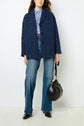 Woman wearing a manteau à chevrons in blue, striped shirt, flared blue jeans, and black shoes, holding a black handbag against a plain white background.