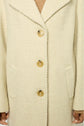 Close-up of a cream-colored manteau à chevrons with three large tan buttons, two front pockets, and part of the person’s hands and neck visible. The person is wearing a light brown top underneath.