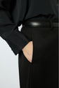 Person wearing black pants and a black shirt with a black belt, standing with one hand in their pocket. The photo is a close-up focused on the waist and hand.