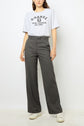 A woman stands against a plain background wearing a light gray graphic t-shirt, high-waisted dark gray polka dot pantalon droit from the collection Studio, and white sneakers. Her right hand is relaxed by her side.