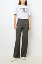 A person stands against a plain background wearing a grey graphic T-shirt, dark high-waisted pantalon droit polka dot trousers from the collection Studio, and white sneakers. Their left hand is relaxed by their side.