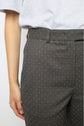 A person wears gray pantalon droit with a small white polka dot pattern from the collection Studio, paired with a light gray t-shirt. Only the lower torso and left arm are visible.