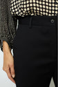 A person wears a cream and black polka dot blouse tucked into high-waisted black pants, with their left hand resting by their side.