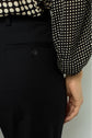A person wearing black trousers and a black-and-white polka dot blouse has their hand resting on their hip. The image shows the back of the trousers and the sleeve of the blouse.
