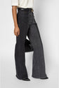Person wearing wide-leg black jean flare pants with front and back pockets, a black belt with a gold buckle, and black pointed shoes. The top is a light short-sleeve shirt. Only the lower body is visible.