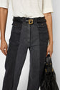 A person wearing a white top, high-waisted denim bicolore jeans with a subtle jean flare and front pockets, a black belt with a gold buckle, and holding a black handbag.