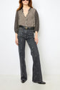 Woman wearing a black and white patterned blouse with three-quarter sleeves, high-waisted dark jeans motif à pois, a double belt, and black shoes, standing against a plain white background.