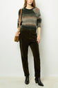 Person wearing a striped green and brown sweater, dark green corduroy pants, black ankle boots, and a brown shoulder bag stands against a plain white background.