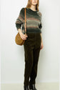 A person wearing a striped sweater, dark olive pants, black ankle boots, and a tan shoulder bag stands against a plain white background.