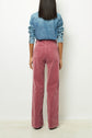 A person stands facing away, wearing a denim jacket and high-waisted, pink corduroy pants. The background is plain white.