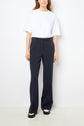 A woman wears a plain white T-shirt tucked into high-waisted, dark navy pantalon tailleur in tissu uni and black shoes, standing against a plain white wall.