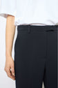 A person wearing a white short-sleeve shirt and high-waisted pantalon tailleur noir en tissu uni, shown from mid-torso to thigh, with one arm relaxed at their side.