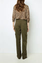 A person stands facing away, wearing an animal print long-sleeve shirt and olive green cargo pants with flap pockets. The setting is minimal with a white background.
