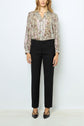 A woman stands against a white background wearing a patterned blouse with long sleeves, black pantalon femme coupe ajustée, and black pointed-toe shoes. Her hands are at her sides and her hair is loose.